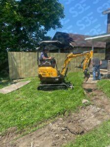 S3E 1-ton excavator with operator digging near a house