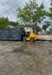 S3E yellow forklift moving a large container on a wet concrete lot