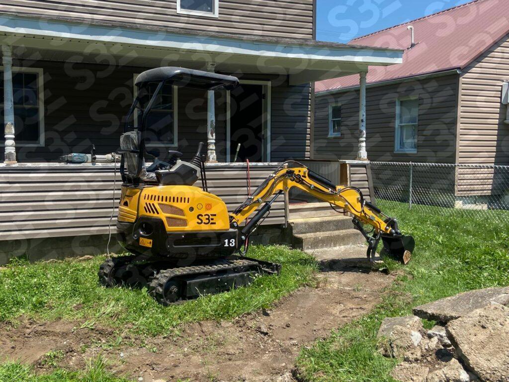 Yellow mini excavator in front of a house with a porch